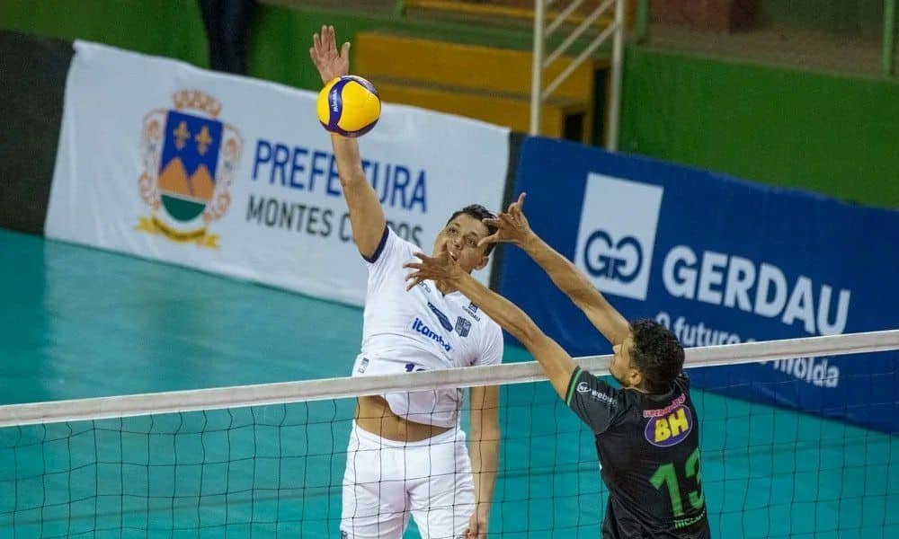 Mineiro de vôlei: Matheus Pinta ataca bola. Ele veste o uniforme branco do Minas. Um jogador do América tenta bloqueá-lo do outro lado da rede