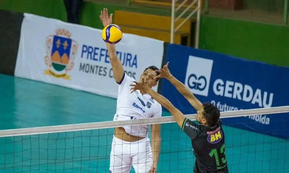 Mineiro de vôlei: Matheus Pinta ataca bola. Ele veste o uniforme branco do Minas. Um jogador do América tenta bloqueá-lo do outro lado da rede