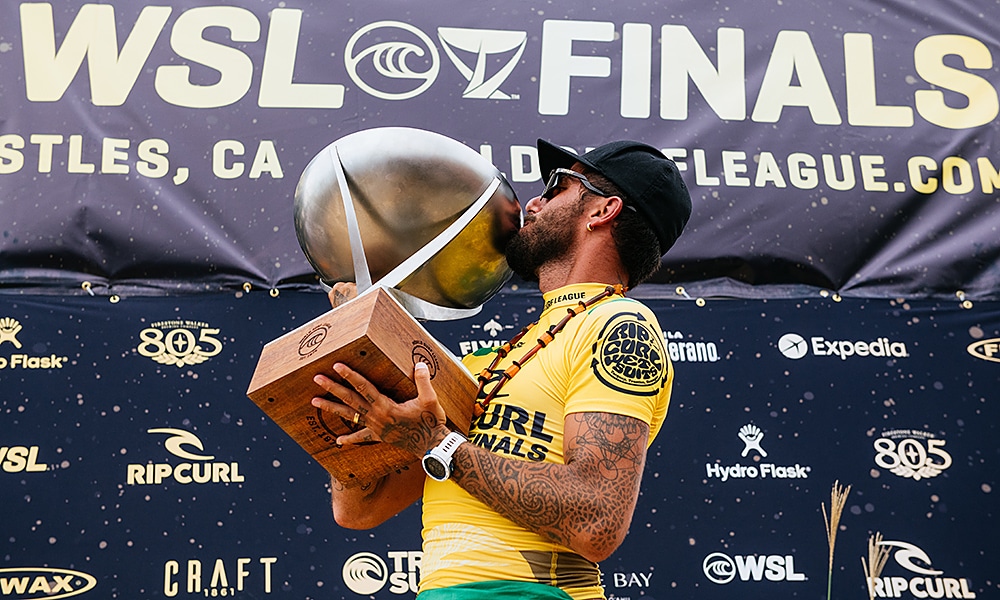 Filipe Toledo WSL Ítalo Ferreira campeão mundial de surfe - Filipinho, vestindo lycra amarela e boné, segura e beija o troféu de campeão