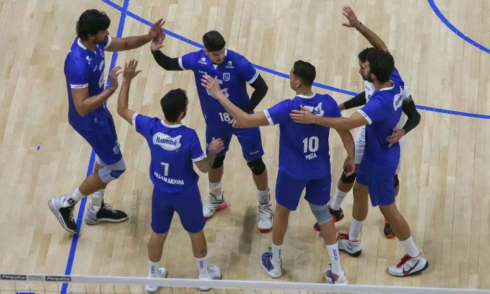 Jogadores do Minas se abraçam após um ponto. Todos vestem uniforme azul royal sobre uma quadra bege
