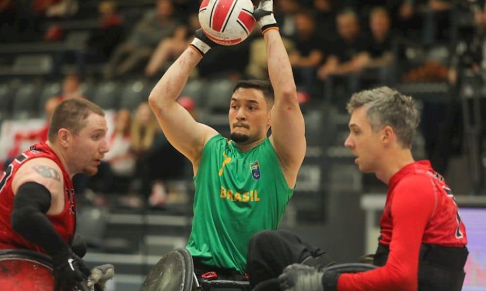Gabriel Feitosa, usando camisa verde do Brasil, conduz a bola entre dois canadenses, usando camisa vermelha / Mundial de rúgbi em CR
