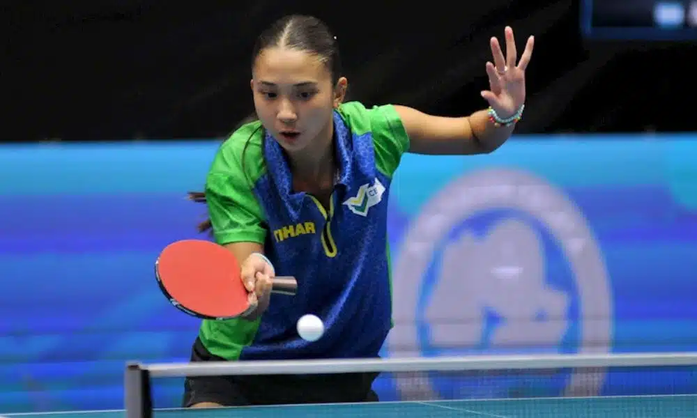 Brasil no tênis de mesa: Giulia Takahashi se prepara para rebater a bolinha. Ela veste uma camisera azul com detalhes em verde Vila Nova de Gaia