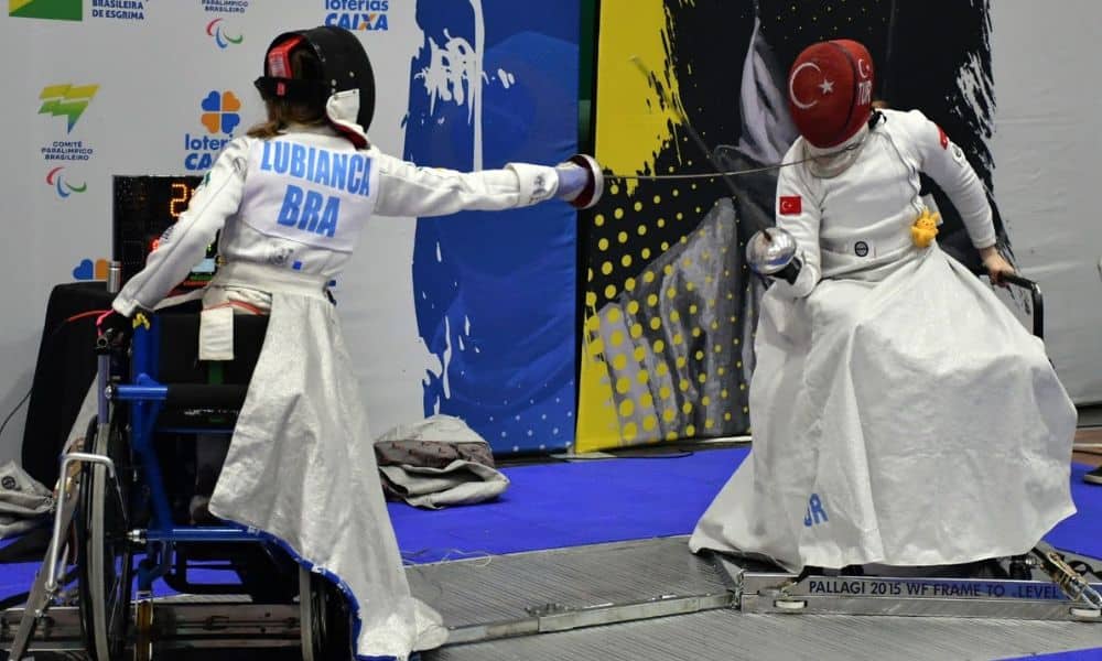 Paula Lubianca, do Brasil, sentada na sua cadeira e apontando espada para esgrimista da Turquia
