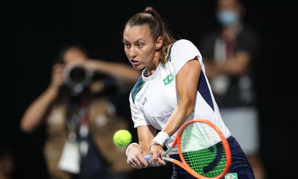 Luisa Stefani, vestindo uma camiseta branca e com cabelo preso, rebate uma bola de forehand