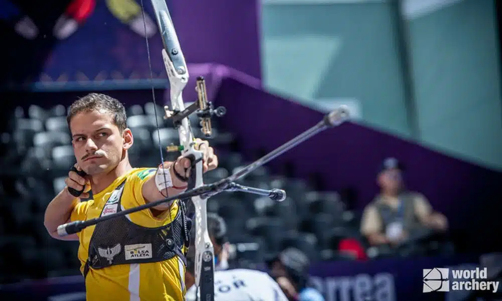 Marcus após soltar flecha do arco. Ele veste uma camiseta amarela e um colete preto para apoiar o arco