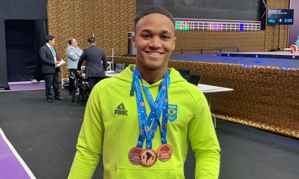 Vestindo um moletom amarelo do Time Brasil, Matheus posa para foto com suas três medalhas no peito