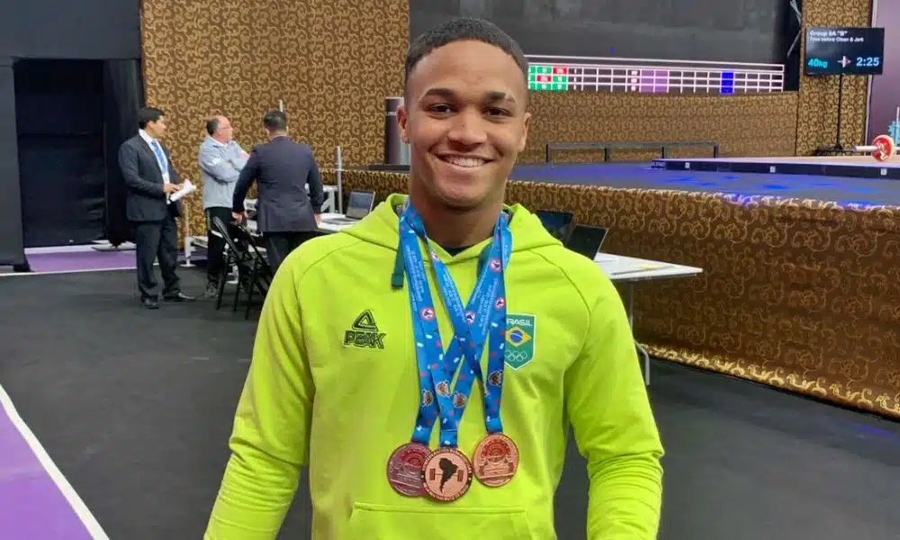 Vestindo um moletom amarelo do Time Brasil, Matheus posa para foto com suas três medalhas no peito