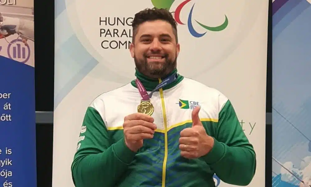 Jovane Guissone posa para foto. Ele segura sua medalha de ouro com uma mão e faz sinal de positivo com a outra