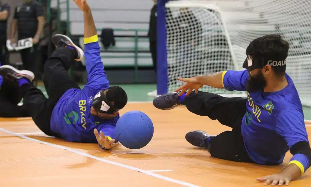 Brasil - dois atletas brasileiros se esticam para fazer defesa. Ambos vestem calças preta e camisa azul