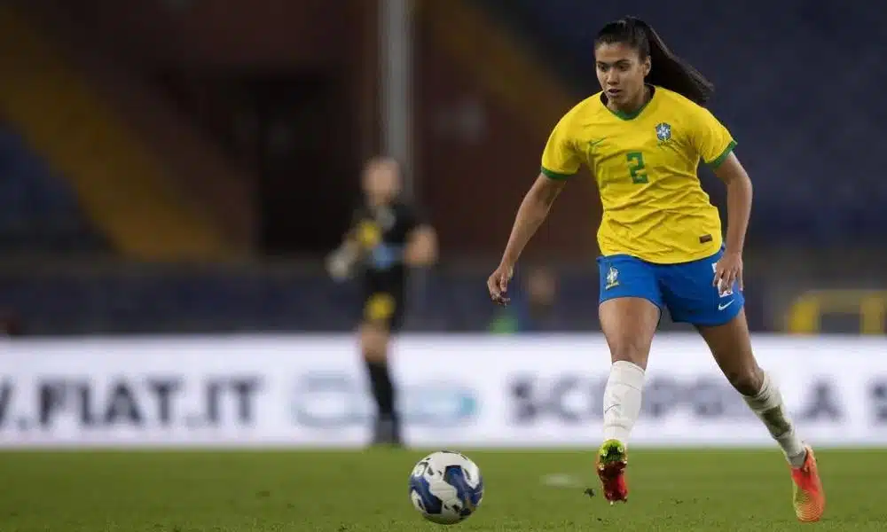 Antônia olha para a bola antes de passe. Ela veste calção azul, camisa amarela número 2 e meiões brancos