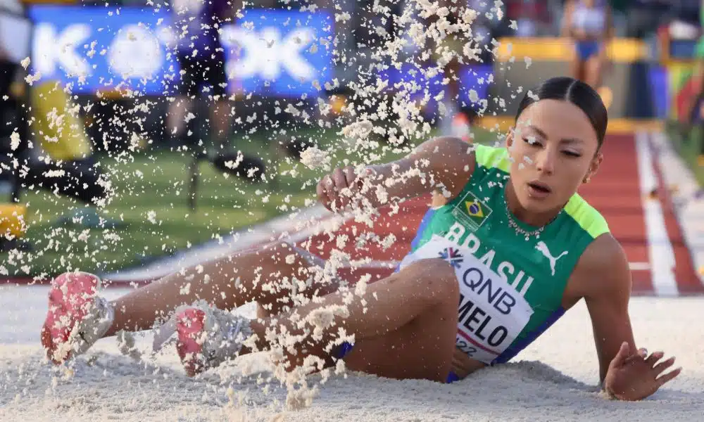 Letícia Oro Melo caindo na caixa de areia do salto em distância. Grãos de areia voam sobre a atleta
