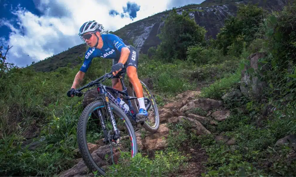 Ulan Galinski, atleta do ciclismo mountain bike, desce em caminho no meio do mato, entre as pedras