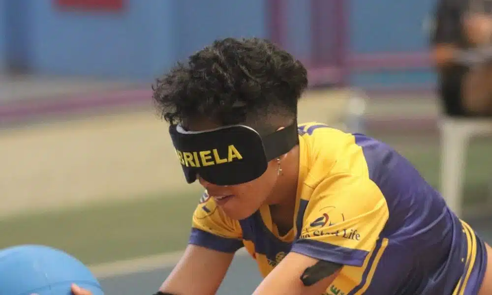 mas Regional de goalball - A jovem Gabriela, de 13 anos, ajeita o corpo para iniciar o movimento de arremesso. Ela tem o cabelo curto e usa uma venda com seu nome escrito