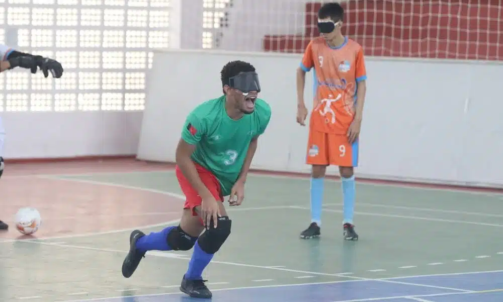 Maicon está se levantando do chão da quadra após comemorar seu gol. Ele grita enquanto apoia o corpo no joelho direito. Veste camiseta verde, calção vermelho e meiões azuis da Apace (Renan Cacioli/CBDV)