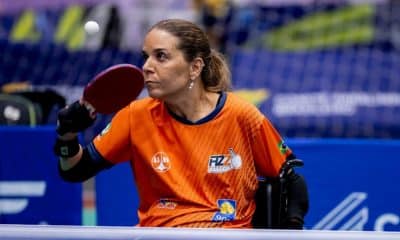 Carla Maia, da classe 2, está na cadeira de rodas com camisa laranja e olha para bola para rebater com a mão direita