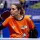 Carla Maia, da classe 2, está na cadeira de rodas com camisa laranja e olha para bola para rebater com a mão direita