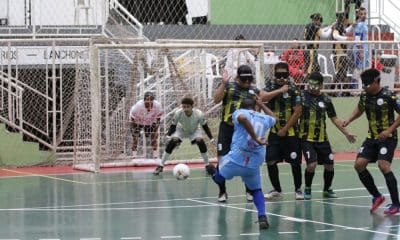 Selmi, da ADVP, chuta de pé esquerdo, a bola vai passando pelo lado da barreira com três atletas da Uniace e, ao fundo, o goleiro Igor aguarda a trajetória da bola com os olhos bem atentos ao lance (Renan Cacioli/CBDV)