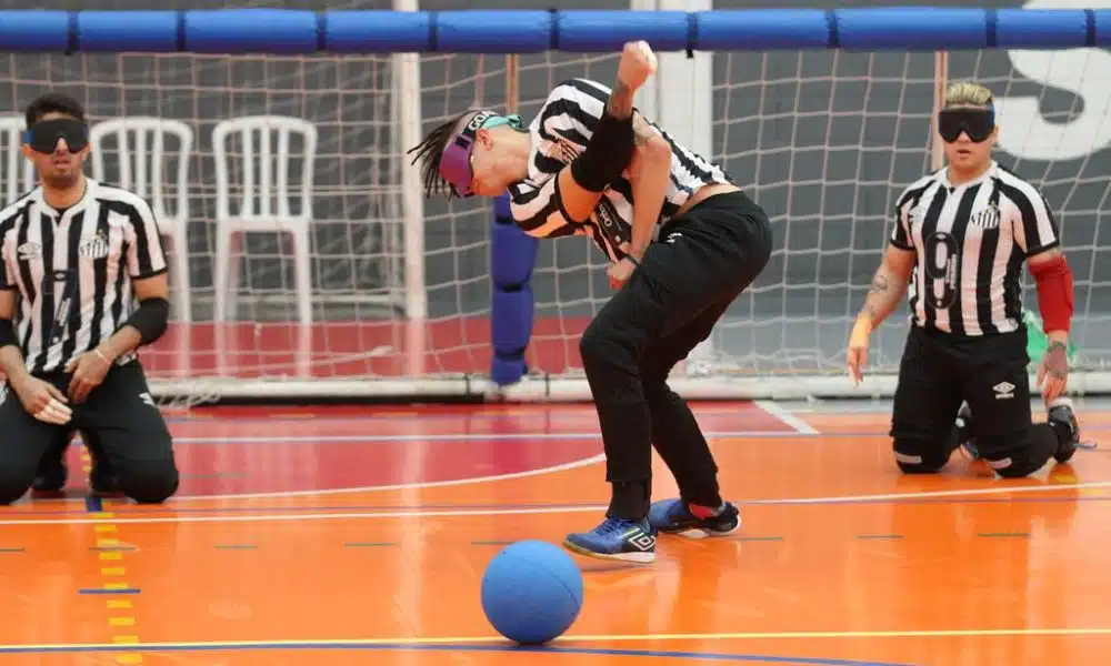 Jogador do Santos faz arremesso em jogo do Regional Sudeste 2 de goalball. Os atletas da equipe vestem calças pretas e camiseta branca e preta listrada