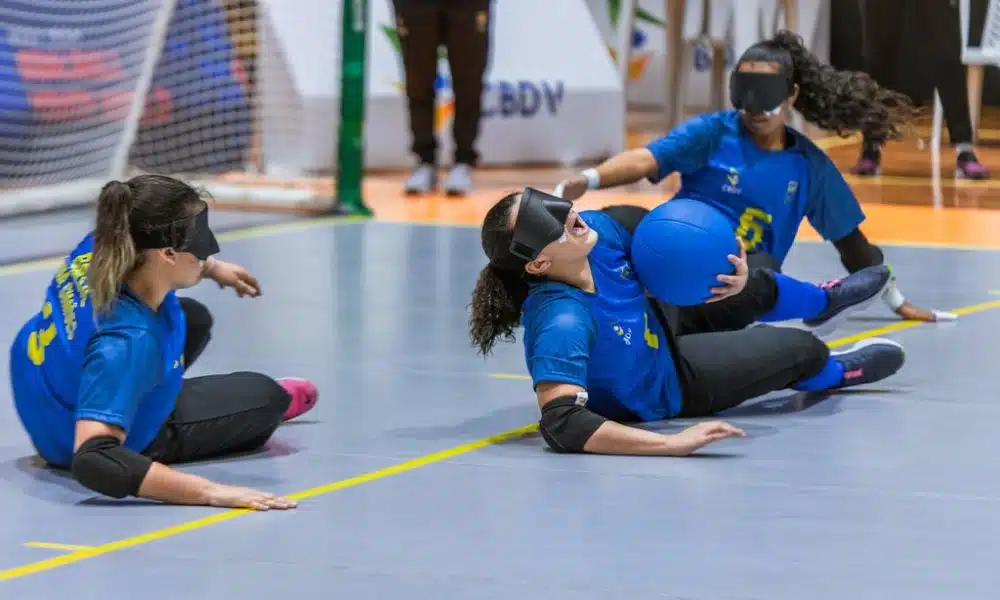 Na posição de pivô, Amanda Braz encaixa a bola no tronco com a mão esquerda enquanto vibra com a boca aberta e o rosto apontado para cima; ao seu lado, Kemilly e Ana Beatriz (Foto: Tuane Fernandes/CBDV)