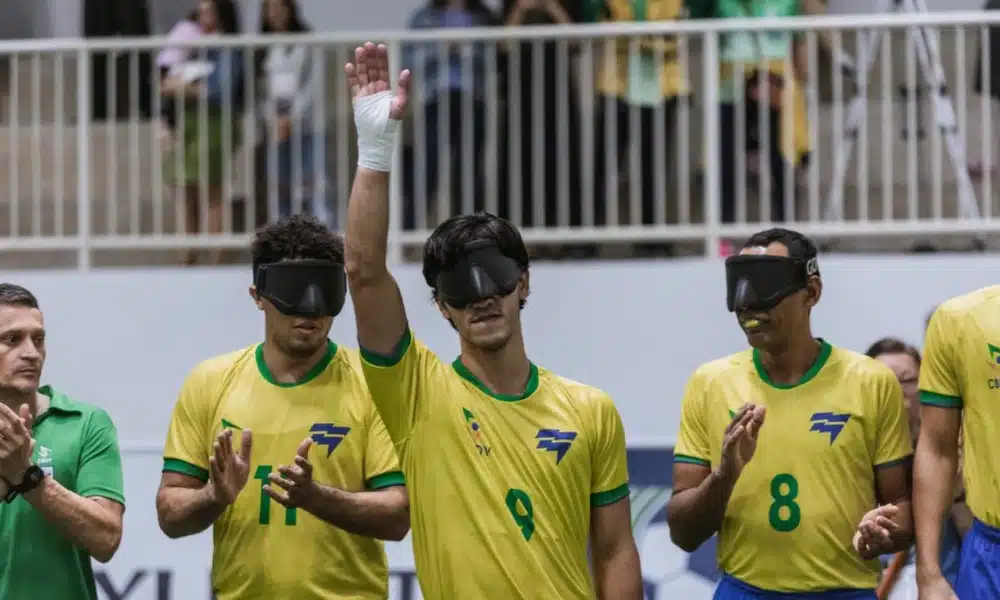 Tiago Paraná ergue o braço direito para saudar o público antes de início de jogo. Ele está perfilado ao lado de Edson, Jardiel e Nonato, que aparecem na imagem