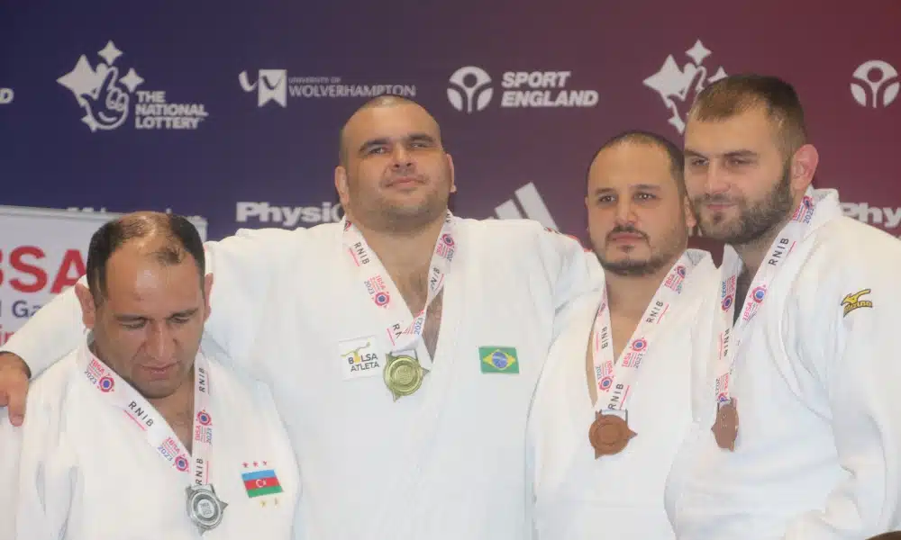 Wilians é o segundo da esquerda para a direita e está abraçado aos outros três judocas no pódio de sua categoria. Wilians é branco, forte e tem o cabelo raspado. Todos os atletas do pódio vestem quimono branco e trazem as respectivas medalhas penduradas no pescoço