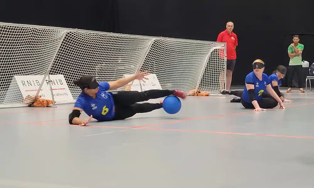 Na imagem, na ala direita do Brasil, Kátia estica as pernas na posição de chicote e defende a bola com os pés; ao seu lado, pivô Gaby aguarda desfecho do lance.