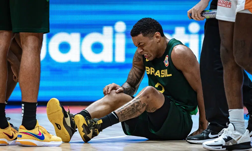 Yago está sentado na quadra, com cara de dor, e coloca a mão no joelho