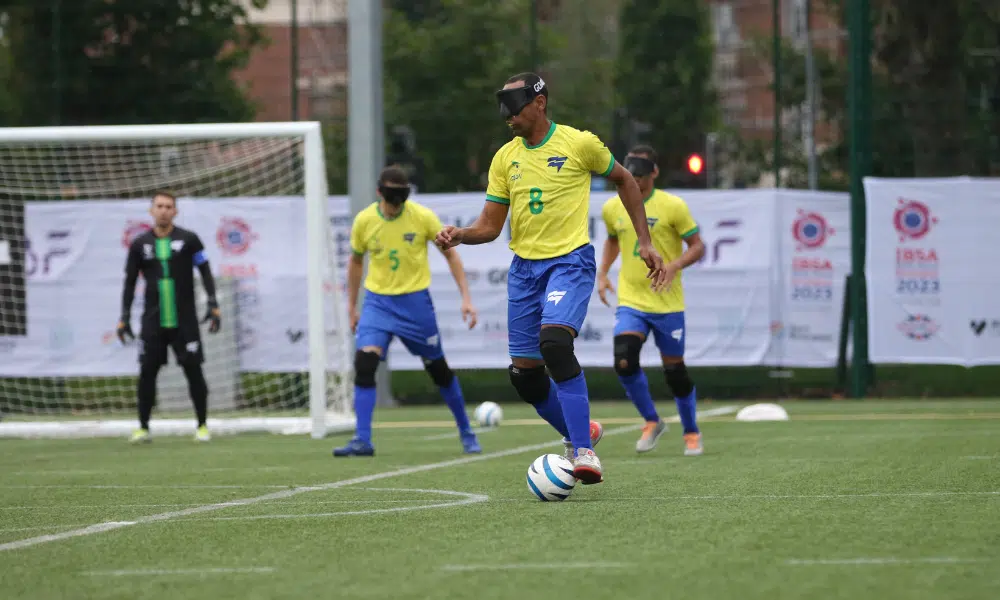 Nonato conduz a bola para o Brasil em jogo da Copa do Mundo. Ele veste calções e meias azuis e camisa amarela do time brasileiro