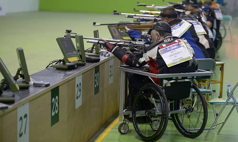 Na imagem, paratleta do Brasil em posição de disparo, com outros atletas ao lado.
