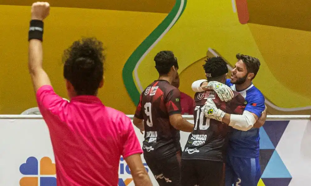 Jardiel é abraçado pelo goleiro Matheus Costa, e está próximo de Jonatan. Do lado esquerdo da foto, árbitra Klévia está com o braço esquerdo erguido e o punho cerrado indicando a marcação do gol (Foto: Taba Benedicto/CBDV)
