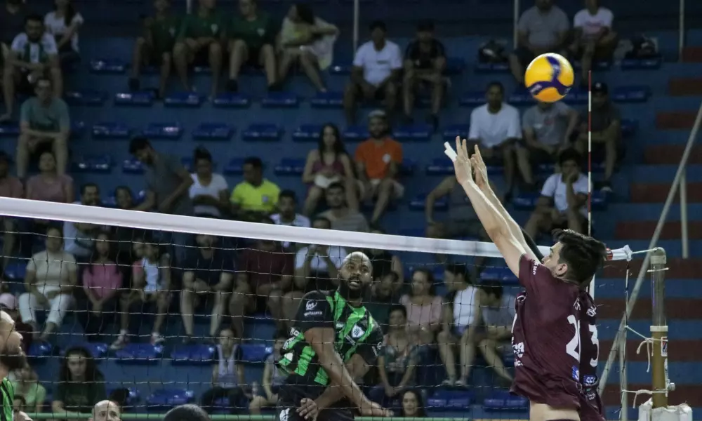 Jogador do América ataca bola contra bloqueio em partida do Campeonato Mineiro de vôlei masculino