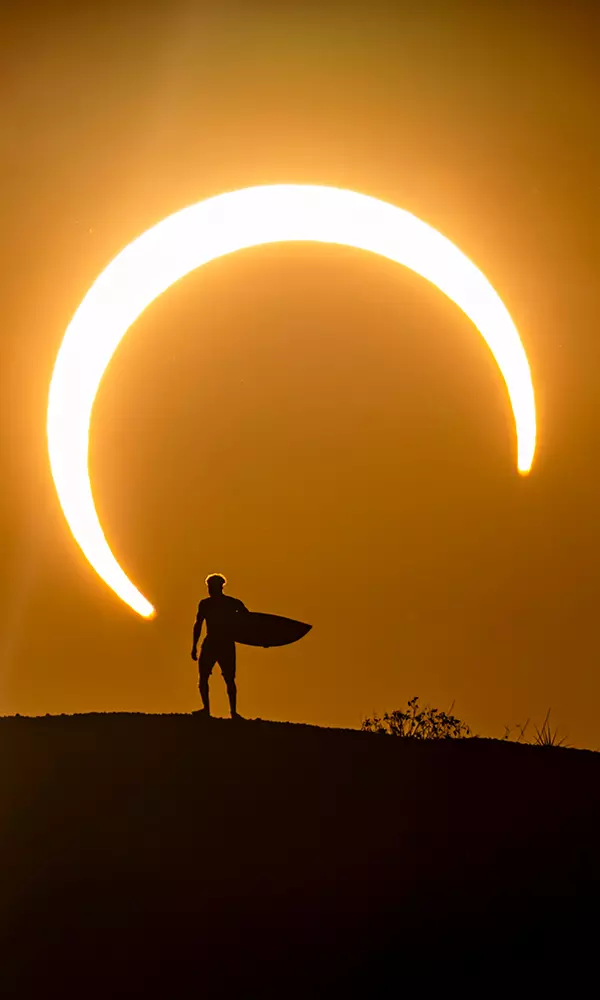 Na imagem, Ítalo Ferreira com sua prancha diante do eclipse solar.