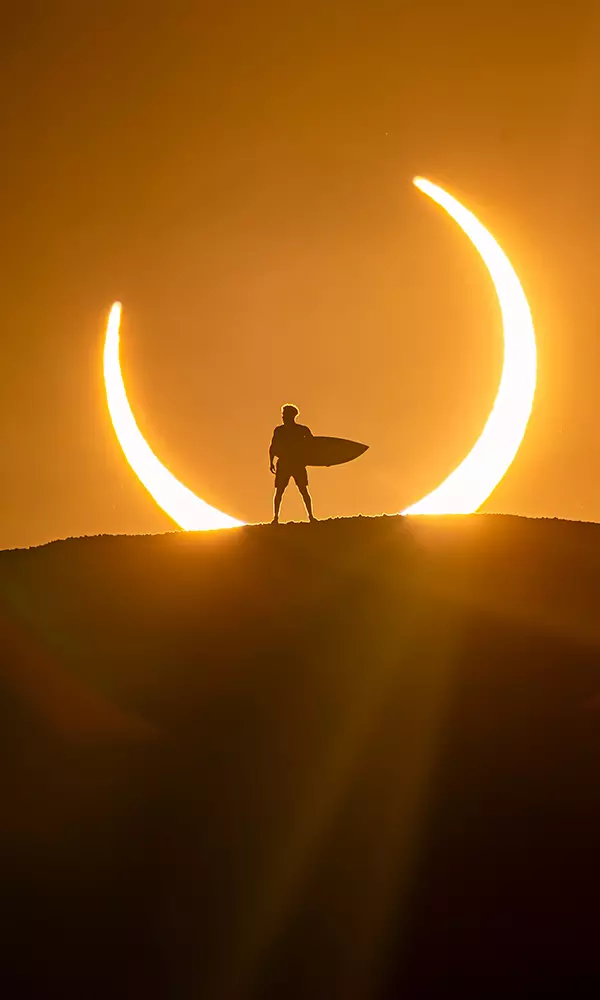Na imagem, Ítalo Ferreira com sua prancha diante do eclipse solar.