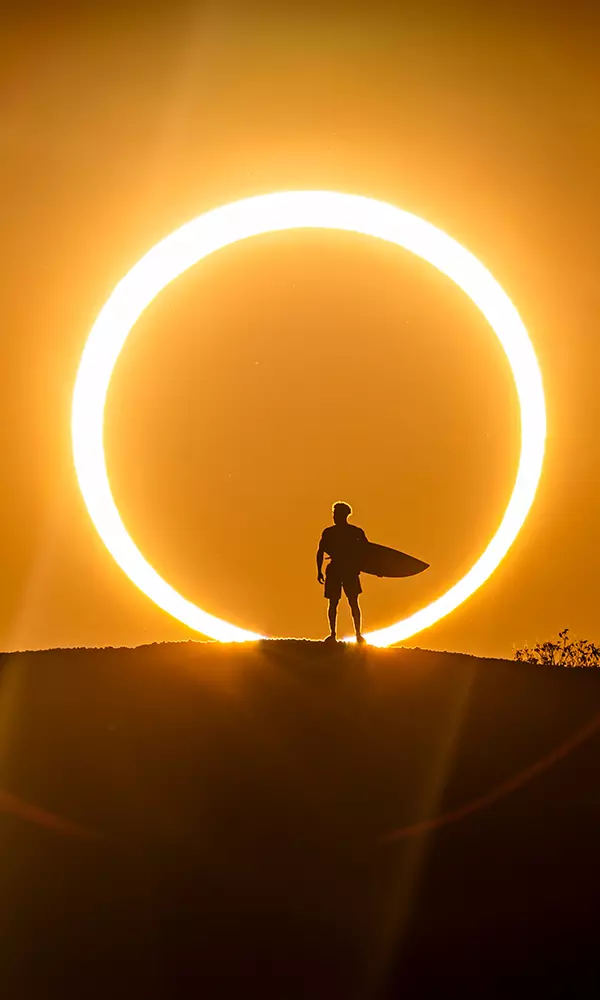 Na imagem, Ítalo Ferreira com sua prancha diante do eclipse solar.