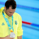 Léo de Deus olha para a medalha de prata, com a cabeça abaixada, em frente à piscina dos Jogos Pan-Americanos