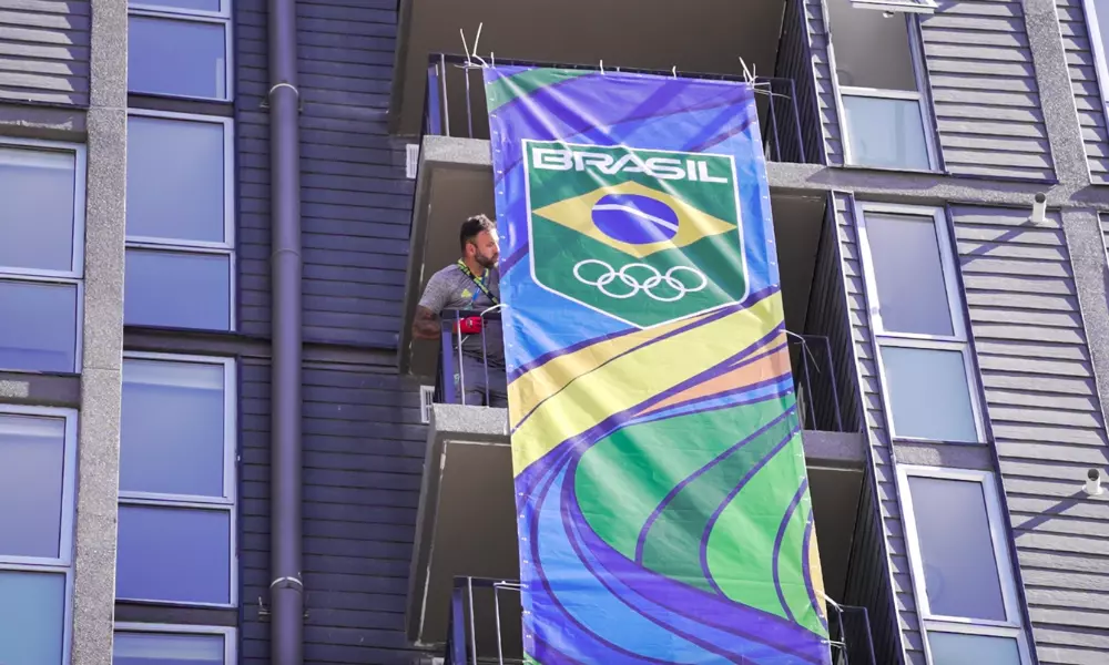 Trabalhador está na sacada de um prédio na Vila Pan-Americana ajustando uma plotagem com a marca do Time Brasil
