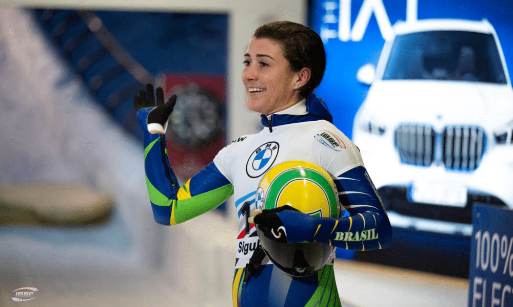 Nicole Silveira está com o capacete na mão, sorri e acena durante Copa do Mundo de skeleton