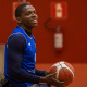 Jogador da seleção brasileira de basquete em cadeira de rodas está de camiseta azul, com a bola na mão, e sorri. Ao fundo, há uma parede vermelha. Ele estará nos Jogos Parapan-Americanos de Santiago-2023.