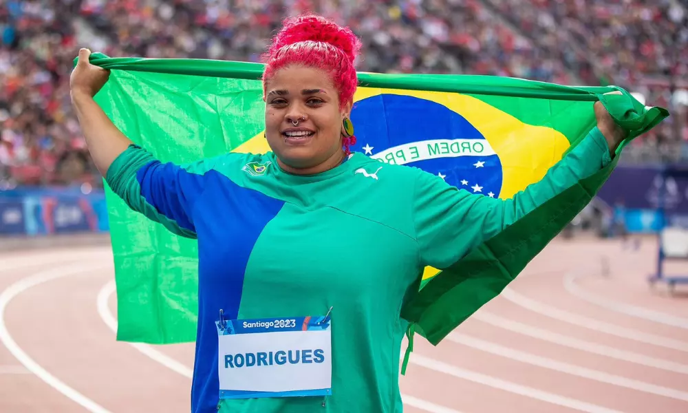 Izabela Rodrigues da Silva com bandeira do Brasil nas costas após medalha de ouro no lançamento de disco em Santiago-2023