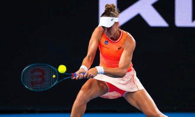Bia Haddad, com uniforme laranja da Asics, rebate bola com backhand no Australian Open. Ela enfrenta Maria Timofeeva ao vivo