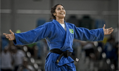 Mariana Silva usa quimono azul enquanto sorri de braços abertos após luta de judô