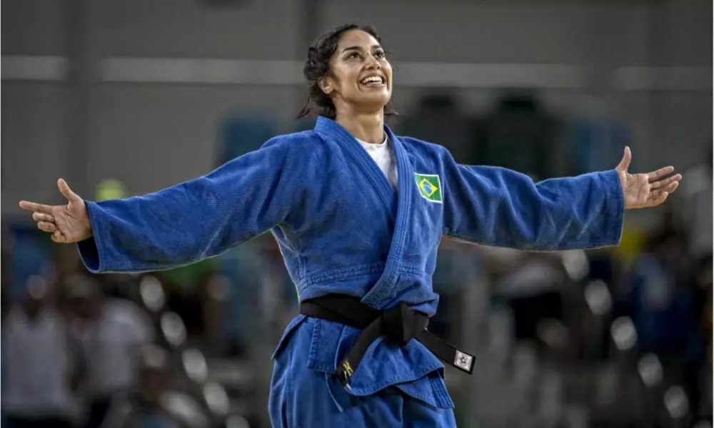 Mariana Silva usa quimono azul enquanto sorri de braços abertos após luta de judô