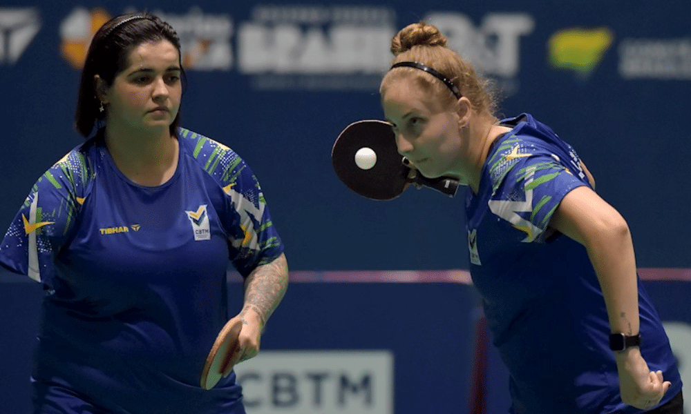 Danielle Rauen saca enquanto Bruna Alexandre observa em partida de tênis de mesa paralímpico