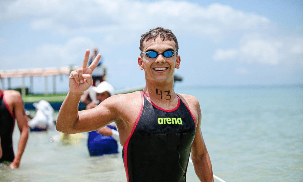 Henrique Figueirinha sorri para foto, em traje de banho, com mar ao fundo, após competir nas águas abertas; ele e Pedro Farias disputaram os 10km no Mundial de Doha
