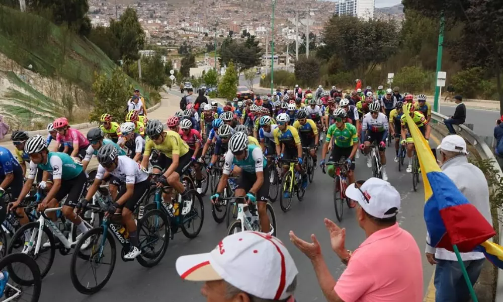 Acima de expectador com camiseta rosa, aparece Victor Paula com uniforme da seleção brasileira em meio ao pelotão na Volta da Colômbia de ciclismo de estrada