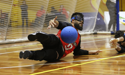 André Dantas cai para o lado esquerdo ao amortecer a bola na defesa com o tronco. Ele veste calça preta e camisa vermelha com mangas longas pretas do Sesi no Regional Sudeste 2 de Goalball