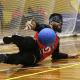 André Dantas cai para o lado esquerdo ao amortecer a bola na defesa com o tronco. Ele veste calça preta e camisa vermelha com mangas longas pretas do Sesi no Regional Sudeste 2 de Goalball