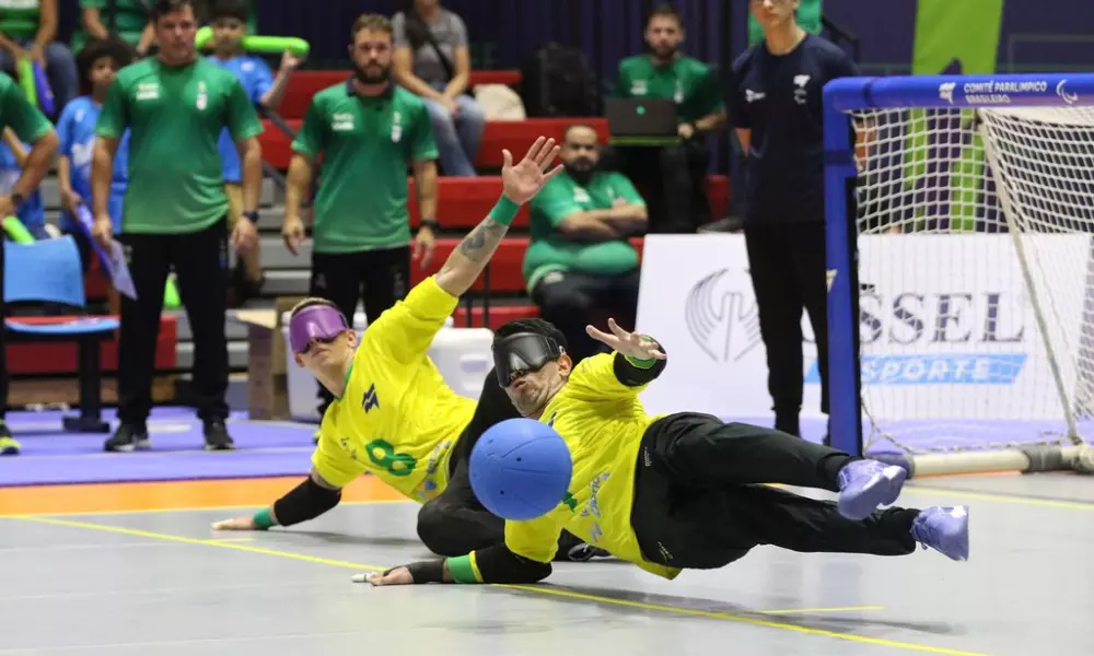 No pivô, Emerson eleva as pernas do chão na posição de chicote e faz a defesa com o tronco. Ao seu lado, Paulinho também executa a posição defensiva, com o braço esquerdo esticado para cima. Ao fundo, comissão técnica olha o lance (Foto: Renan Cacioli/CBDV)