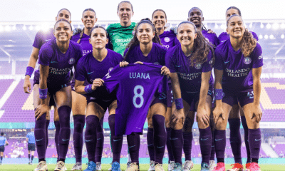Jogadoras do Orlando Pride posam para foto segurando camisa de Luana Bertolucci antes de jogo da NWSL