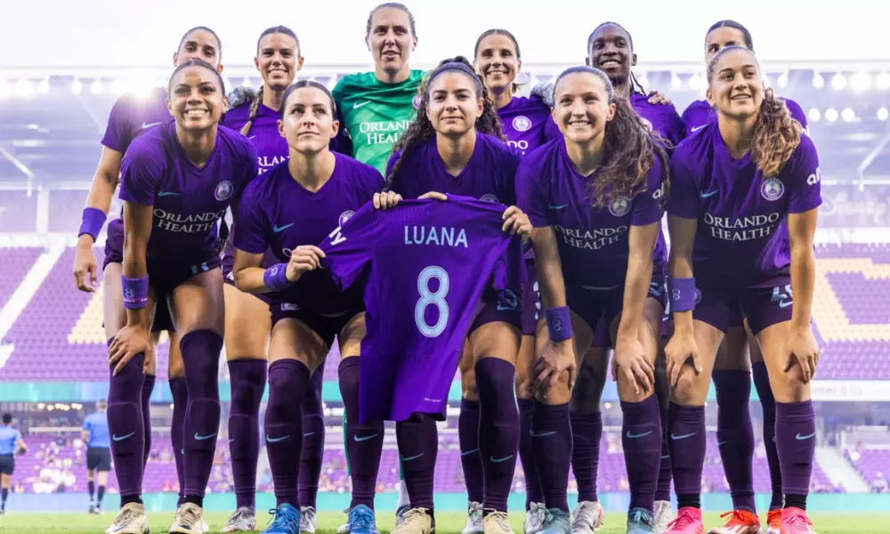 Jogadoras do Orlando Pride posam para foto segurando camisa de Luana Bertolucci antes de jogo da NWSL